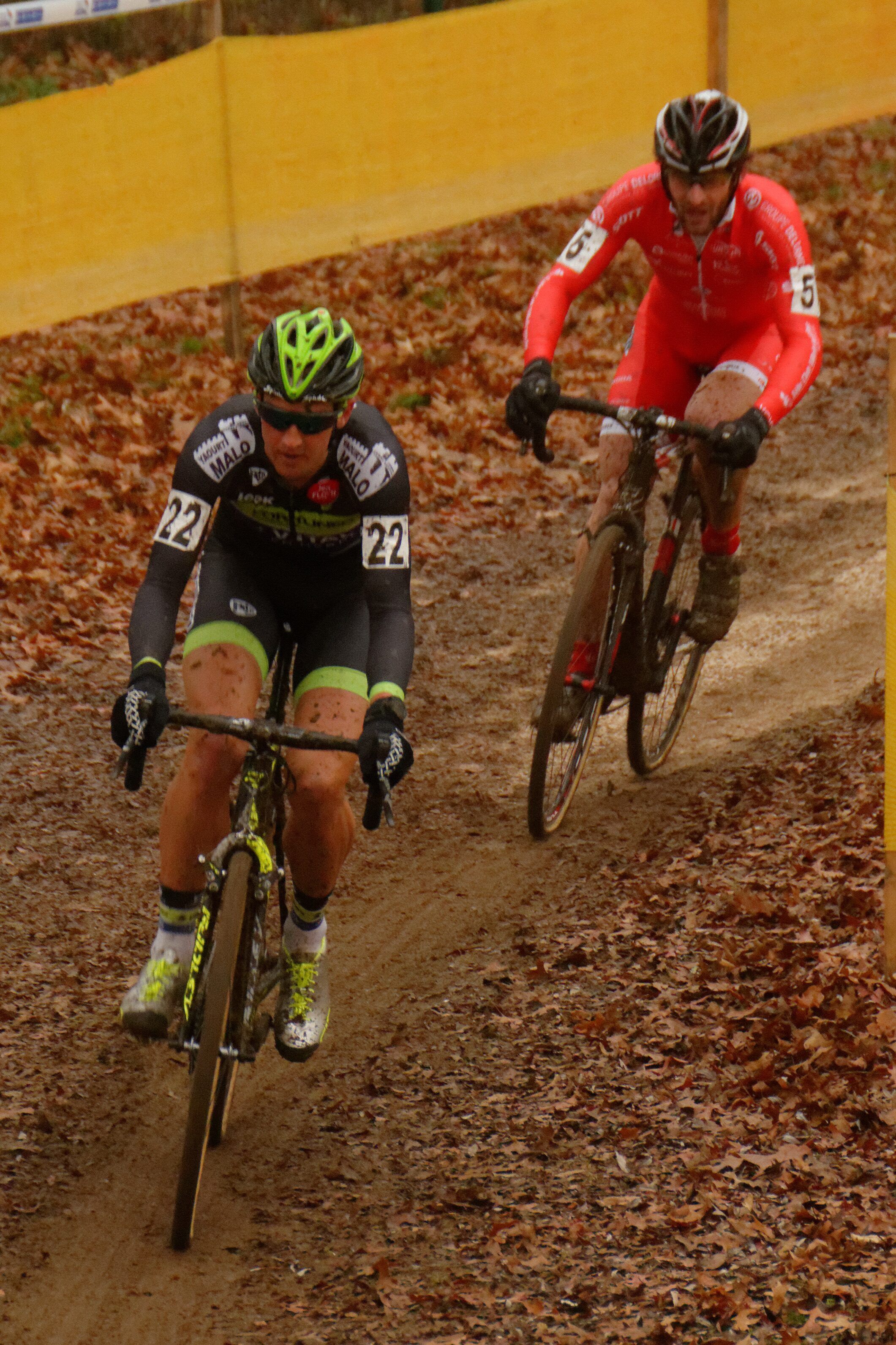 Deux coureurs descendent un chemin de terre couvert de feuilles mortes, l'un derrière l'autre, entre des rubans jaunes.